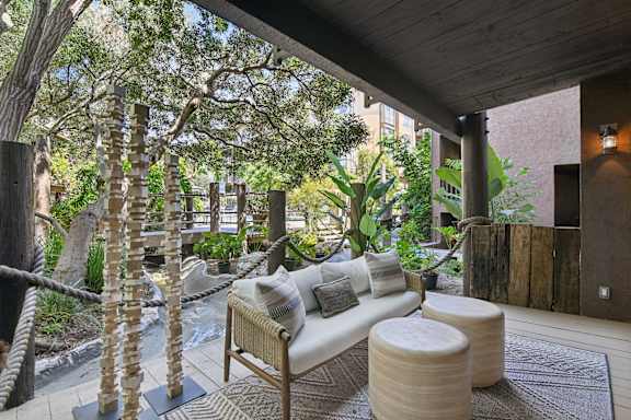 A wooden sofa with cushions sits on a rug in a room with a wooden ceiling and a tree trunk on the left.