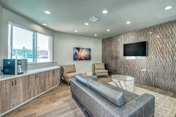 A modern waiting room with a grey sofa, wooden cabinets, and a television mounted on the wall.