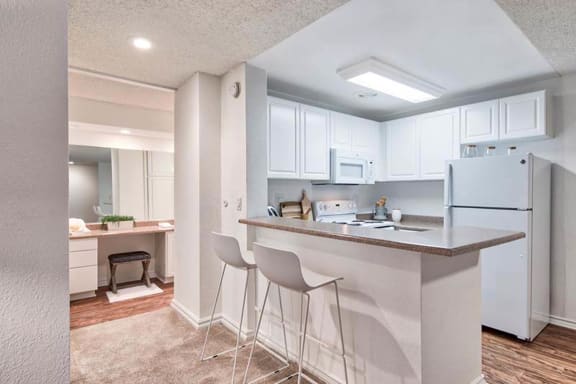 a kitchen with white cabinets and a bar with two stools at The Meadows Apartments, Culver City, CA