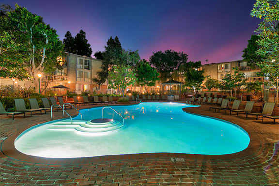 A swimming pool surrounded by lounge chairs and trees at The Meadows Apartments, Culver City