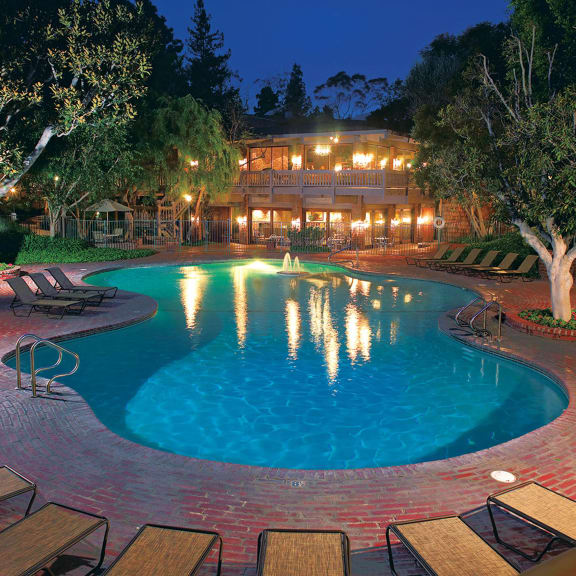 a large swimming pool with chairs around it at night at The Meadows Apartments, Culver City