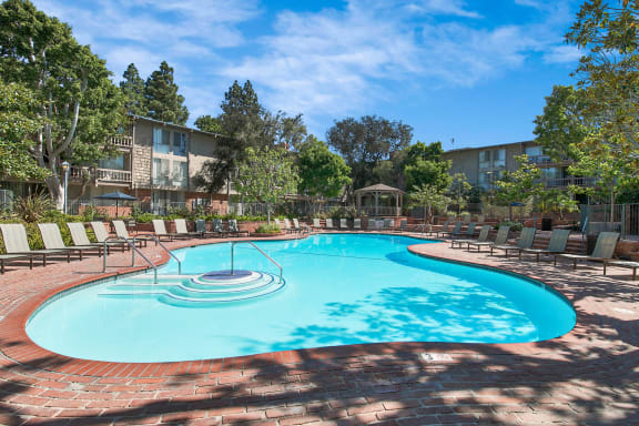 a resort style pool with chairs and a building in the background at The Meadows Apartments, Culver City