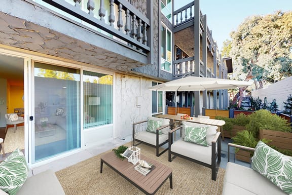 A patio with a table and chairs and a white umbrella at The Meadows Apartments, Culver City, CA