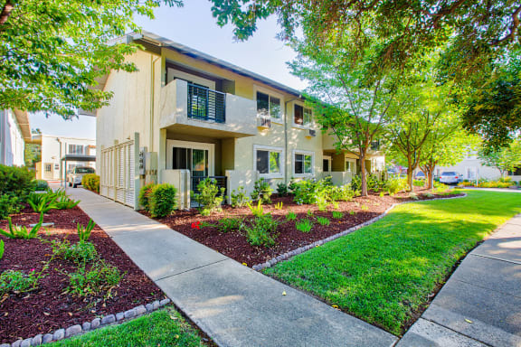 a sidewalk in front of a building with grass and trees  at Pleasanton Place, Pleasanton, CA