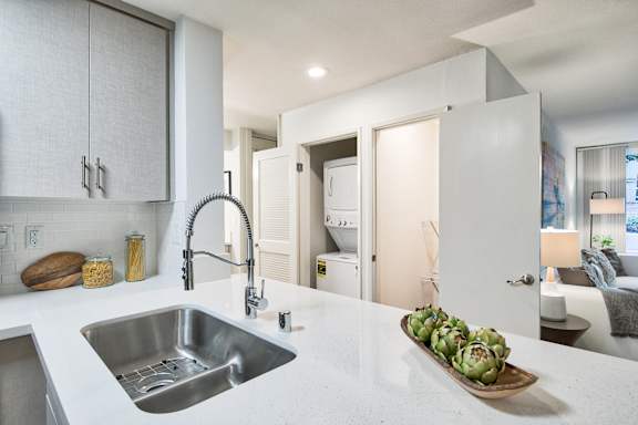A modern kitchen with a stainless steel sink and a wooden cutting board with artichokes on it at The Meadows Apartments, Culver City , CA