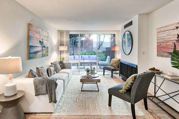 A living room with a white couch, a coffee table, and a large painting on the wall at The Meadows Apartments, Culver City , CA