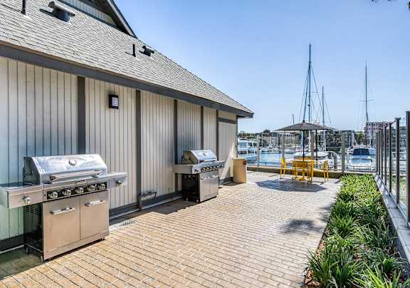 A barbecue grill is on a wooden deck next to a building.