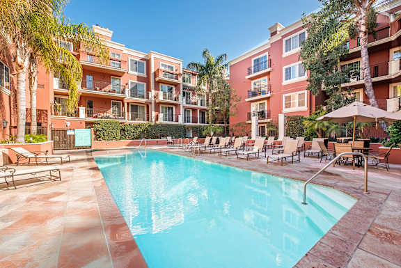 A swimming pool surrounded by lounge chairs and umbrellas in front of a red building at Marina Harbor, Marina del Rey, California