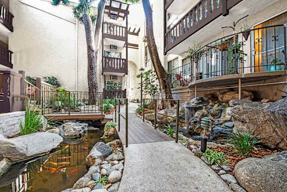A small pond with rocks and a wooden bridge in the middle of a courtyard at Mediterranean Village West Hollywood, West Hollywood