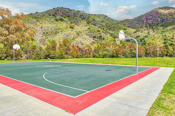 A basketball court with a red and green surface and a mountain in the background.