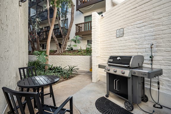 A black grill is on a patio with a table and chairs at Mediterranean Village West Hollywood, California