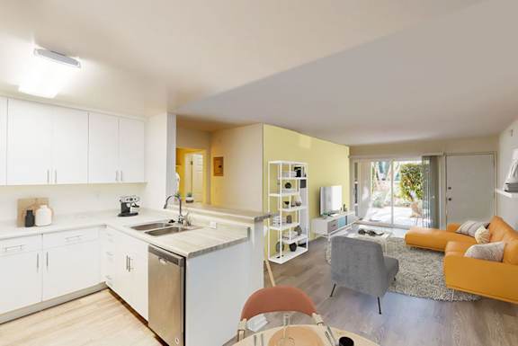 A modern kitchen with white cabinets and a dining area with a grey couch and orange cushions.