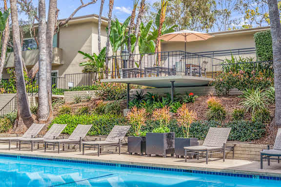 A pool surrounded by lounge chairs and trees.