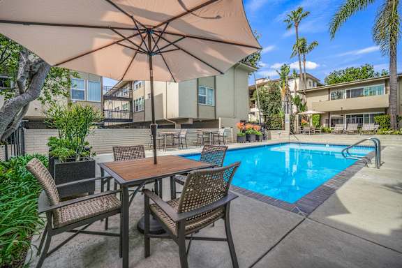 A patio with a table and chairs under an umbrella next to a pool.