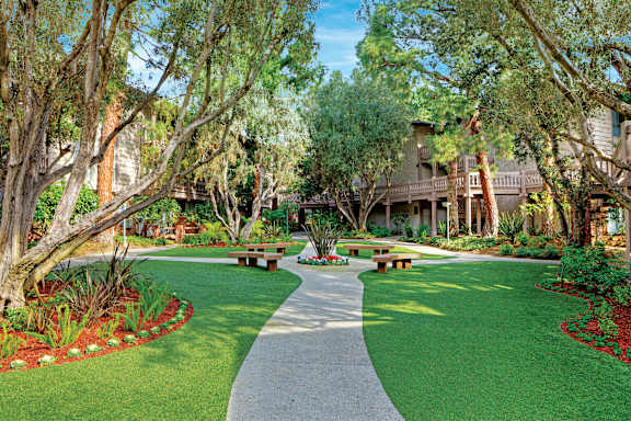 A walkway in a park with benches on either side at The Meadows Apartments, Culver City , CA