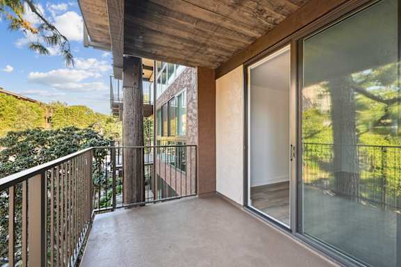 A balcony with a glass door and a view of trees.