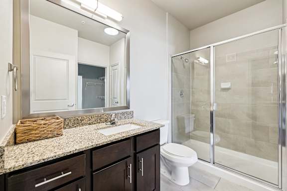 A bathroom with a toilet, sink, mirror, and shower. at North Creek, Texas