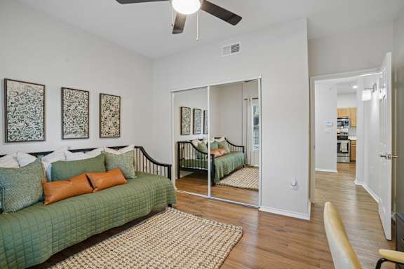 A bedroom with a green couch and a mirrored closet door.
