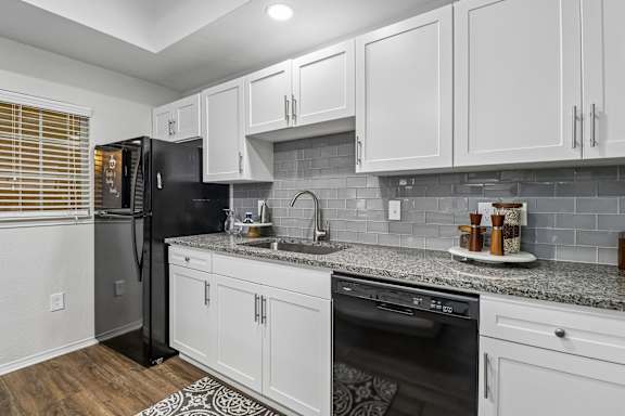 A kitchen with white cabinets and a black refrigerator.