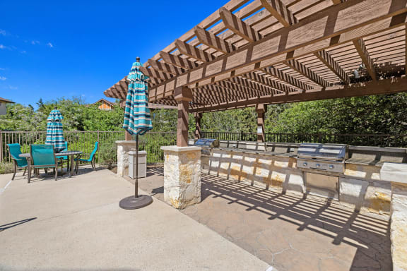a patio with a pergola and table with umbrellas at Lakeline East Apartments, Texas