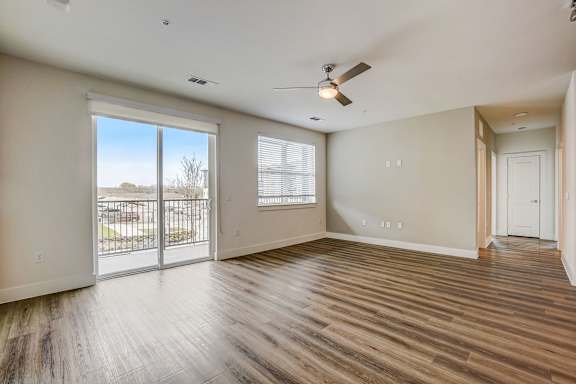 A room with a sliding glass door leading to a balcony, hardwood floors, and a ceiling fan.