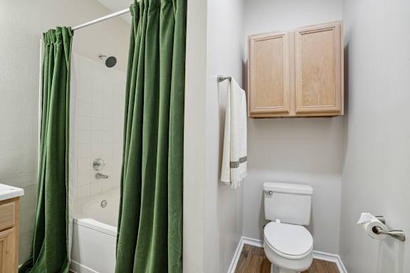A white toilet sits next to a white bathtub with green curtains.