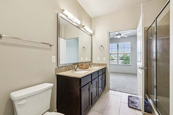 A bathroom with a white toilet, a sink with a mirror above it, and a glass shower door.at North Creek, Hutto, TX, 78634