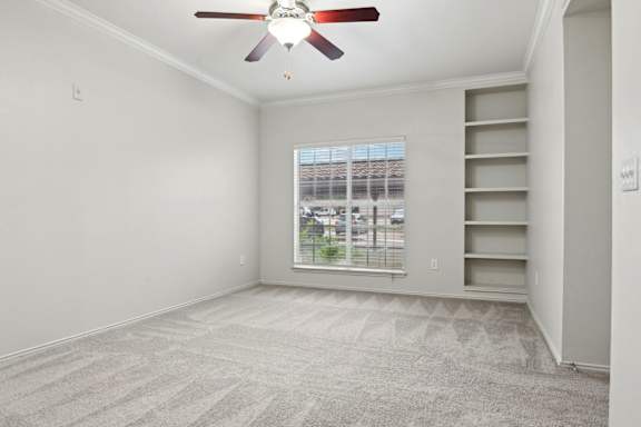 A room with a ceiling fan and a window overlooking a parking lot.