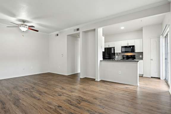 A room with a ceiling fan and a kitchen area with a microwave, oven, and refrigerator.