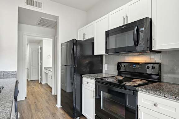 A black refrigerator and microwave in a kitchen with white cabinets.