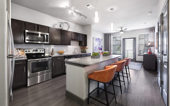 a kitchen with stainless steel appliances and a large island with chairs at North Creek, Texas, 78634
