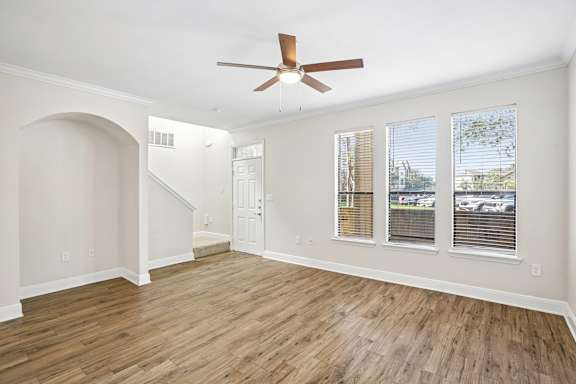 A room with a fan, wooden floors, and a staircase.