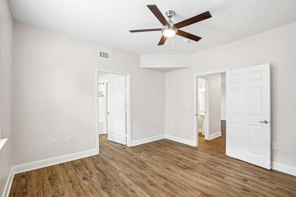 A room with a ceiling fan and wooden floors.