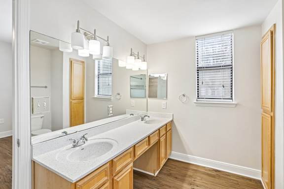 A bathroom with a large mirror, a sink, and a window with blinds.