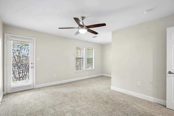 A room with a ceiling fan and a door leading to a balcony.