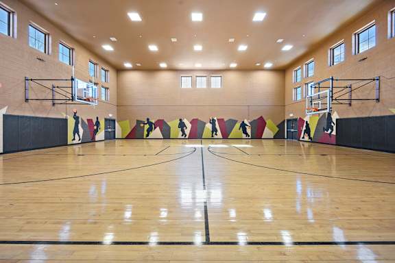A basketball court with a wooden floor and a wall with a mural of basketball players.