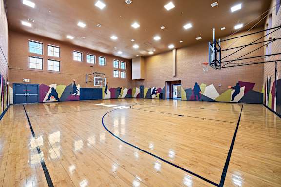 A gym with a wooden floor and a basketball hoop.