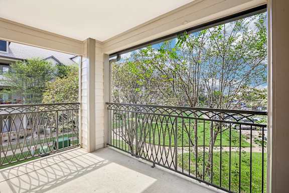 A balcony with a metal railing and a view of a green lawn and trees.