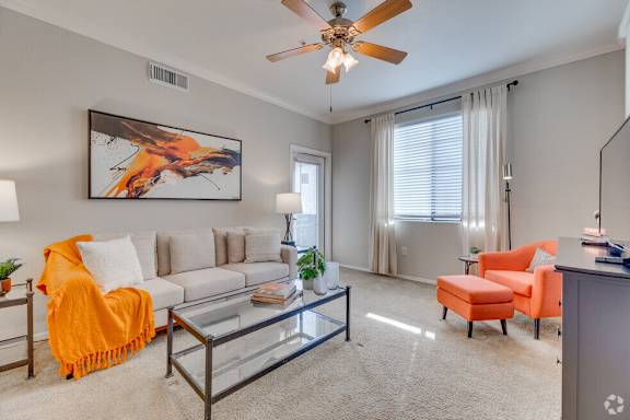 A living room with a white couch, orange chair, and a painting on the wall.