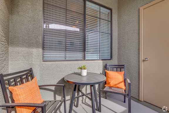 A small table with two chairs and a potted plant sits on a patio.