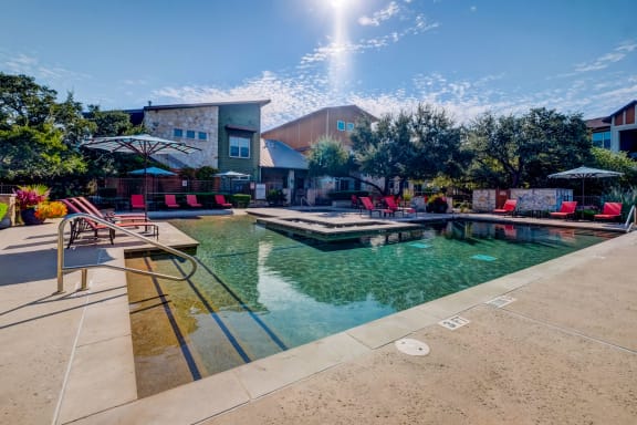a resort style pool with lounge chairs and umbrellas at Lakeline East Apartments, Texas
