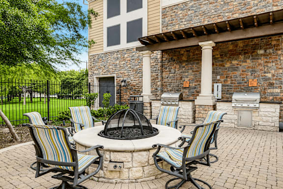 A patio with a fire pit and chairs.