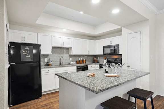 A black fridge in a kitchen with white cabinets.