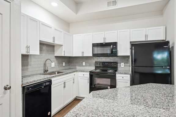 A kitchen with black appliances and white cabinets.