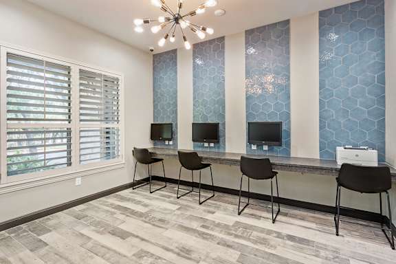 a room with a long desk with three computers on it and a chandelier hanging from at Sonterra Apartment Homes, Austin, TX, 78726