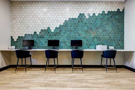 Three chairs are placed in front of a desk with a laptop on it. at Ventana Oaks Apartments, Austin, TX
