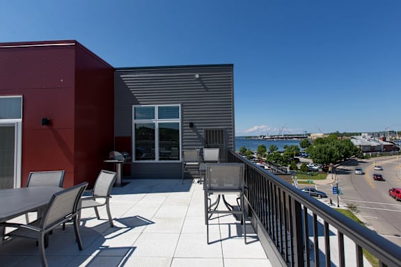 A balcony with a table and chairs overlooks a street and a mountain.
