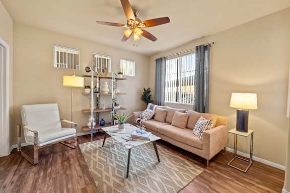 A living room with a white chair, a beige couch, and a ceiling fan.