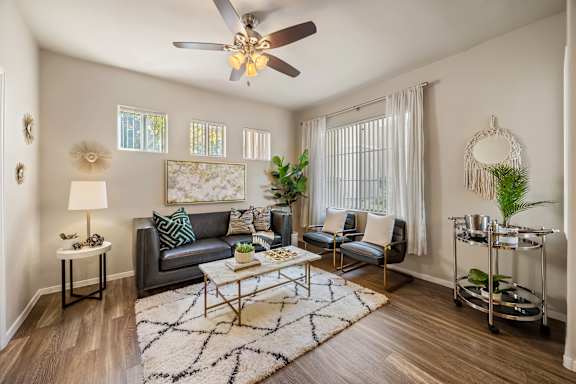 A living room with a grey couch, a coffee table, a ceiling fan, and a rug.