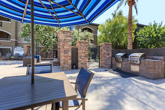 a patio with a table and chairs and a blue and white umbrella at The Preserve by Picerne, N Las Vegas, 89086